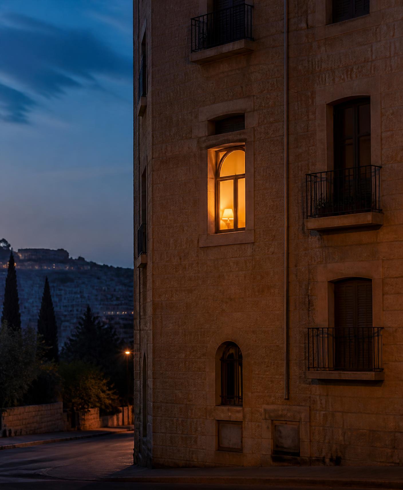 A warmly lit window in a Jerusalem stone building at dusk, representing The Lighthouse supportive home for young women