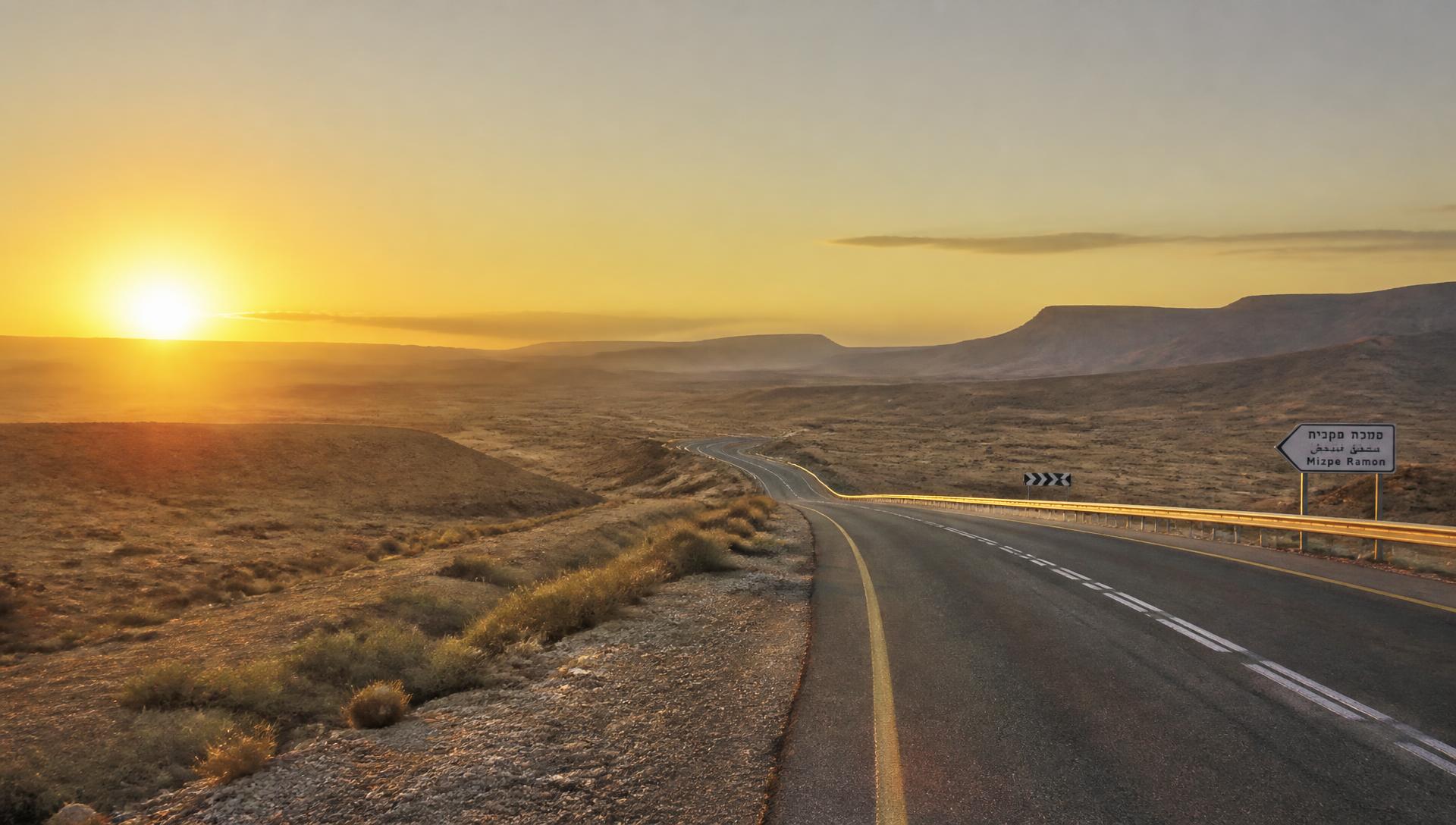 An open desert highway curving toward distant hills at sunrise in Israel